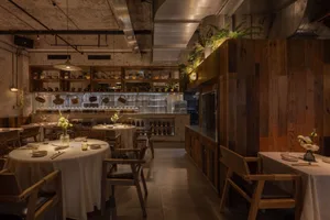 Empty restaurant interior with wooden floors and walls, featuring dining tables with wine glasses and vases