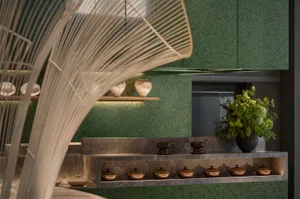 A modern kitchen with green walls and countertops, featuring variously sized bowls and a potted plant, emphasizing functionality and organization