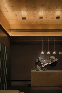 A warm and inviting room with a large stone wall, brown tone, and three lights providing illumination, with a bowl placed on a surface near the center