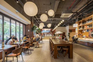 A casual dining area in a restaurant with a large wooden table surrounded by chairs, soft lighting, and a mix of wood and metal elements