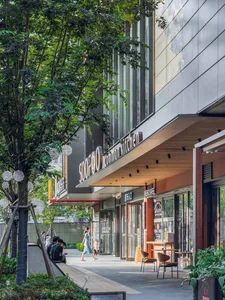 Modern restaurant with a glass front, wood accents, and natural light from a large window, set in an urban street scene with people walking by