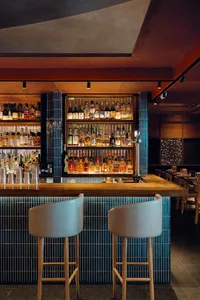 A bar area in a restaurant with a wooden countertop, stools, and bottles on display, creating a warm and inviting atmosphere