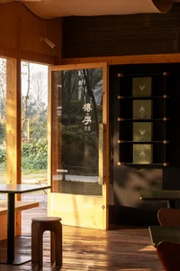 Warm and inviting Asian restaurant with wooden floors and walls, featuring a large window and dining area with chairs and a table