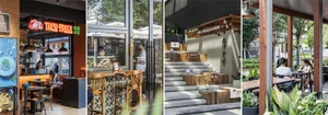 A lively restaurant interior with a wooden staircase, dining tables, chairs, and potted plants, with people sitting and standing around