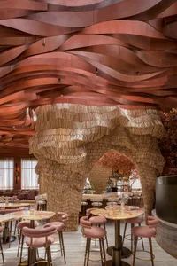 A modern restaurant with wooden walls and ceiling, featuring multiple dining tables and chairs, and warm lighting