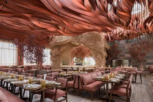 A modern restaurant with wooden walls, multiple tables, chairs, and potted plants, creating a warm and inviting atmosphere