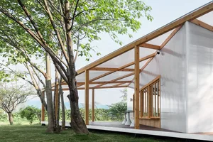 Open living area with a large white building, wooden deck, benches, dining table, and chairs, featuring a bright and inviting atmosphere