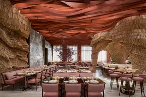 Warm and inviting restaurant interior with wooden walls and ceilings, featuring multiple tables and chairs, potted plants, and a comfortable dining area