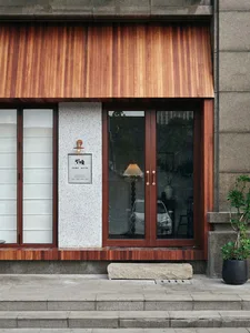 Exterior building facade with a wooden doorway, stone base, and large window allowing natural light to enter