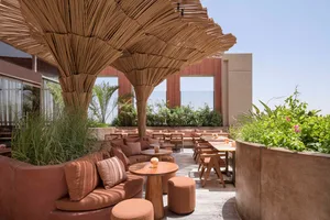 A restaurant patio area with a large straw or reed umbrella providing shade for dining tables and comfortable seating for guests