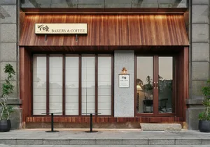 木質外觀的烘焙咖啡店，配有兩張餐桌、椅子與盆栽，背景明亮