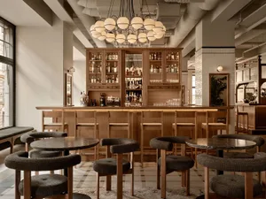 A cozy bar area with wooden tables and chairs, featuring bottles and a warm atmosphere for socializing and enjoying drinks