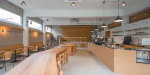 A cozy restaurant interior with wooden floors and tables, multiple chairs, and a large central table surrounded by smaller ones, creating a clean and inviting atmosphere for social gatherings