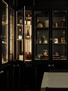 A dark kitchen with cabinets, countertops, bottles, wine glasses, and a bowl, creating a cozy and inviting atmosphere