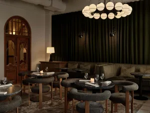 A cozy living space with a couch, chairs, tables, and lamps, featuring wine glasses and soft lighting