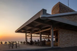 A lively restaurant interior with wood and stone features, multiple tables, and people seated and standing, bathed in natural daylight