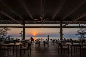 Outdoor restaurant with modern seating, concrete, wood, and metal materials, and warm lighting near a body of water