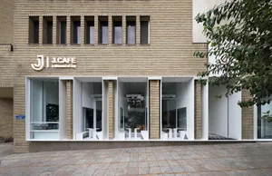 Exterior view of a cafe with yellow brick facade, large window, outdoor seating, and potted plants