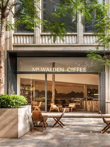 A relaxed outdoor cafe with wooden chairs and tables, accompanied by benches, set in front of a building