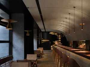 A restaurant or bar area with a long counter and chairs, bottles on display, and a relaxed atmosphere