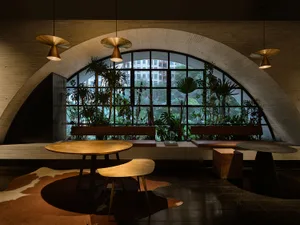 Dining area with a wooden table and chairs, surrounded by a large window for natural light, creating a warm and inviting atmosphere