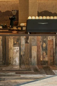 A kitchen scene with a wooden countertop, a black coffee maker, and several cups and bowls placed around it
