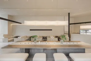 Empty restaurant interior with a wooden dining table and white chairs, surrounded by potted plants and a warm atmosphere