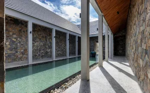 An indoor pool area with stone walls, empty pool, and lounge chairs in a luxurious and sophisticated environment