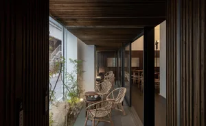 A modern restaurant interior with wooden floors and walls, well-lit and inviting, featuring chairs, dining tables, and potted plants
