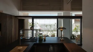 A kitchen with a central island, two chairs, a dining table, potted plants, and a bowl on the countertop