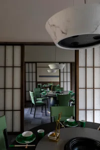 A modern restaurant interior with Asian-inspired decorations, dark wood flooring, and dim lighting, featuring tables, chairs, and tableware