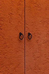 A simple doorway with an orange wall and two black door handles or hinges