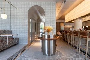 A modern restaurant dining area with multiple tables and chairs, featuring a unique tile pattern on the walls and warm lighting creating a cozy ambiance