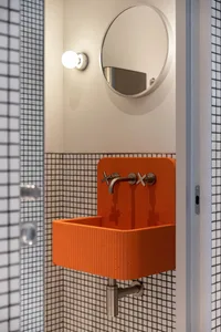 A modern bathroom with a white tiled floor and walls, featuring an orange bathroom sink with two faucets on either side
