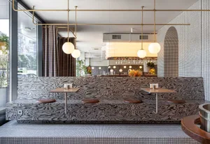 Modern restaurant interior with a bar, dining table, chairs, and unique patterned walls, accented with bottles and ambient lighting