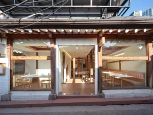 Modern restaurant interior with wooden floors and walls, dining tables, and chairs, featuring wood accents and well-designed lighting