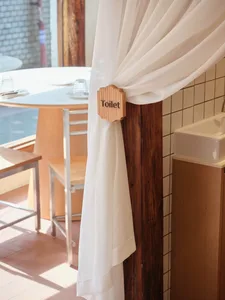 A clean and organized bathroom with a wooden door, white curtain, two chairs, and three cups, featuring a cozy atmosphere