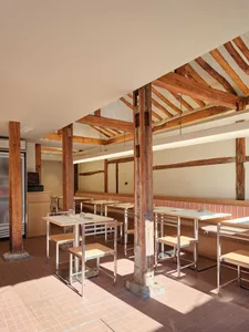 Rustic restaurant with wooden floors and walls, featuring dining tables, benches, and comfortable seating for guests