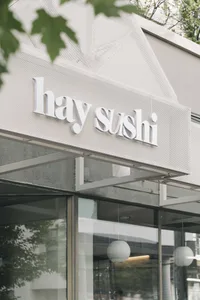 Exterior view of a modern sushi restaurant with a white facade and a glass front, allowing natural light to enter