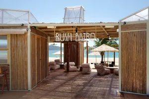 Open-air restaurant with a wooden structure, large roof, and umbrellas providing shade to the seating area