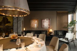 Elegant living room with a dining table, chairs, couch, and lamp, surrounded by wine glasses, creating an inviting atmosphere