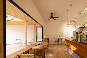 Modern restaurant interior with a bar area, dining space, potted plants, wood flooring, and white walls