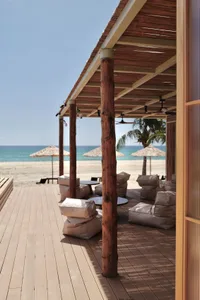 A beach house with a wooden deck overlooking the ocean, featuring chairs and umbrellas for a comfortable seating area