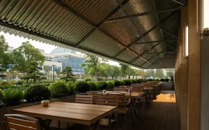 An outdoor dining area with wooden tables and chairs, benches, and nearby trees, creating a comfortable and inviting atmosphere for al fresco meals