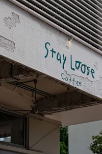 A cozy coffee shop with a white concrete exterior, a green sign reading Stay Loose Coffee, and a welcoming atmosphere