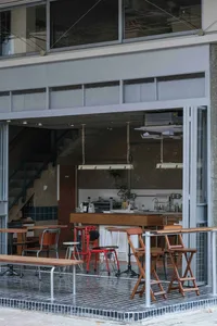Modern restaurant interior with dim lighting, white walls, and wooden flooring, featuring a dining area with tables and chairs and a kitchen area