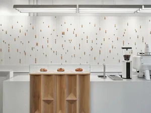 Industrial kitchen with wooden cabinets, white walls, and glass display cases showcasing bread and a coffee maker