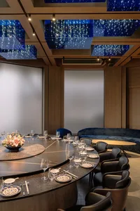 A dining space with a large wooden table and multiple chairs, set with wine glasses, plates, and cutlery, creating an elegant atmosphere