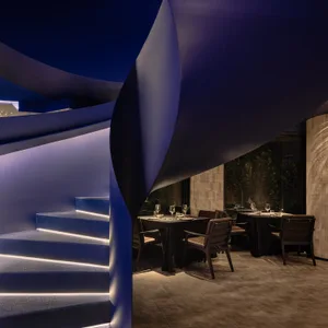Elegant restaurant interior with a spiral metal staircase, tables, chairs, and wine glasses, creating an upscale and inviting atmosphere