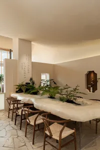 A modern restaurant interior with a long dining table, potted plants, and vases, creating a welcoming atmosphere